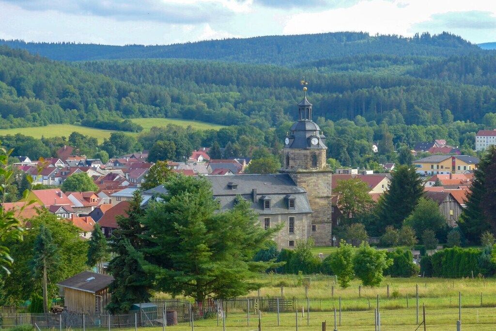 A town with a prominent church tower, surrounded by residential buildings and lush greenery.