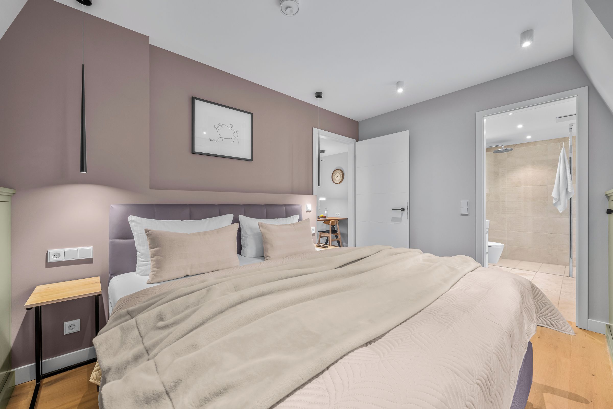 A modern bedroom with a large bed, bedside tables, a framed artwork, and a bathroom with a shower.