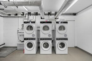 Una sala de bugaderia amb vàries rentadores de la marca Siemens, conductes de ventilació i un sòl de rajola.