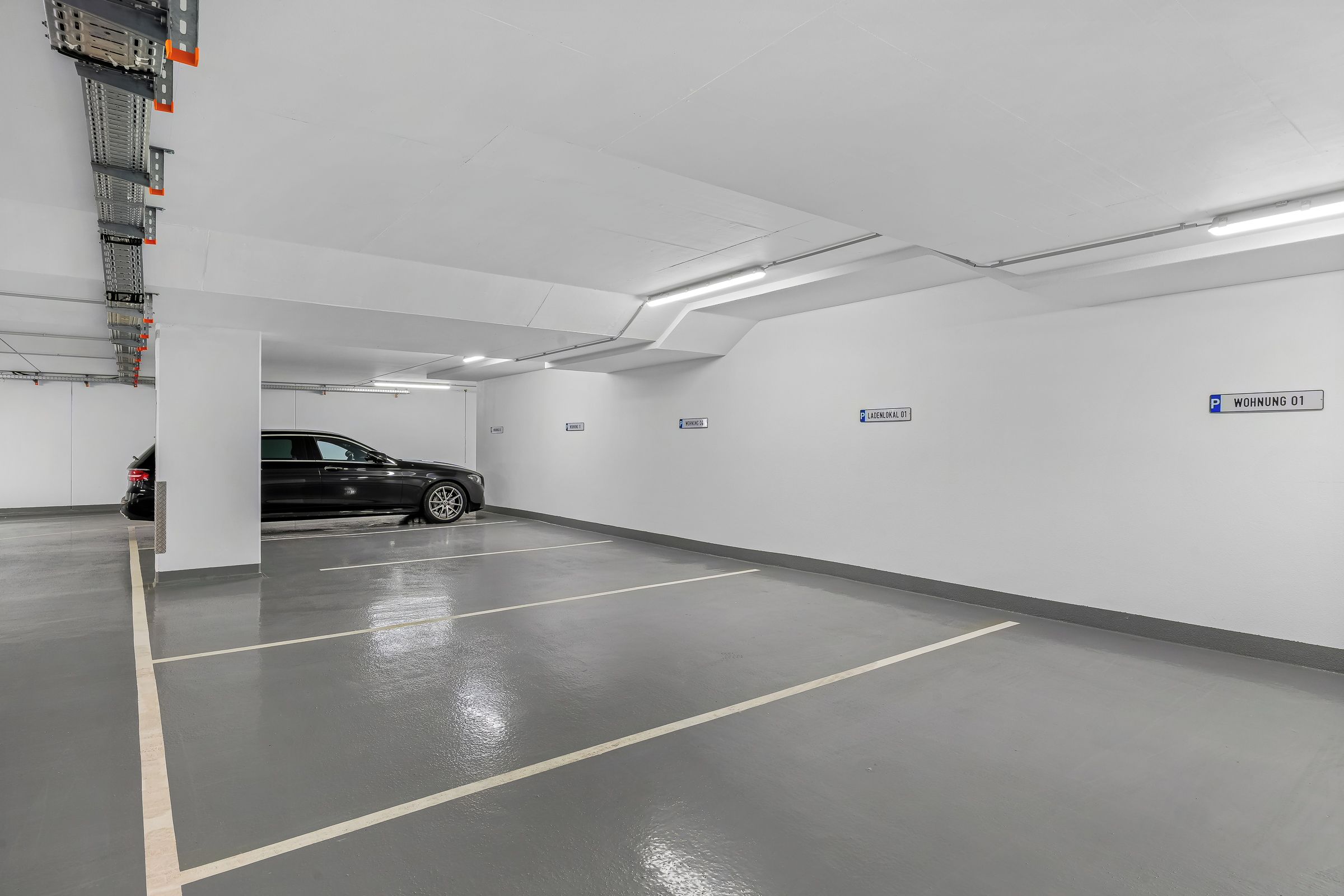 A parking garage with marked parking spaces, a car parked inside, and directional signs.