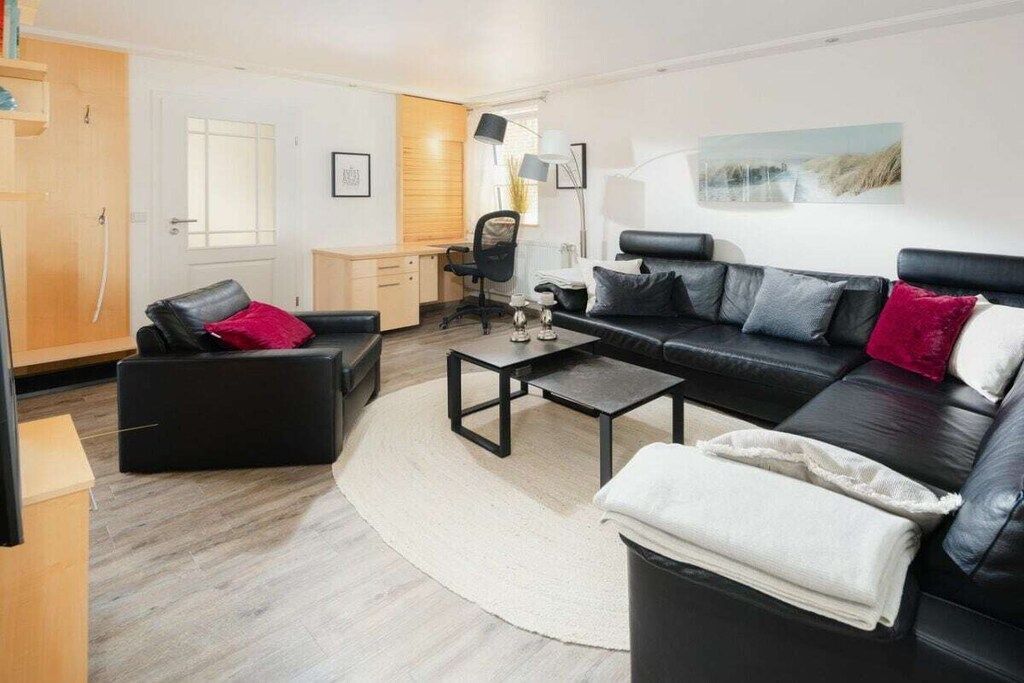 A modern living room with a black leather sofa, a coffee table, and a desk with a chair.