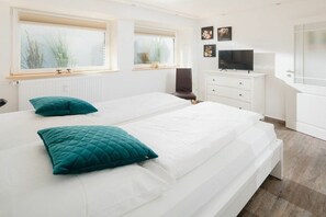 A bedroom with two beds, a dresser, a television, and a window with blinds. - Holiday apartment in Juist with swimming pool (Juist)