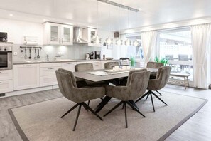 A modern kitchen with white cabinetry, a dining table with four chairs, and a large window with curtains. - Holiday apartment in Juist with swimming pool (Juist)