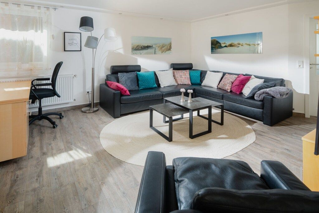 A modern living room with a black leather sofa, a coffee table, and a desk with a chair.