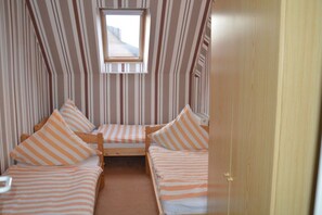 A room with three single beds, each with striped bedding, a window, and a door. - Holiday apartment with 3 bedrooms (Neuschoo)