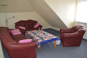 A small room with a brown leather sofa, a matching armchair, and a small table with a floral tablecloth. - Holiday apartment with 3 bedrooms (Neuschoo)