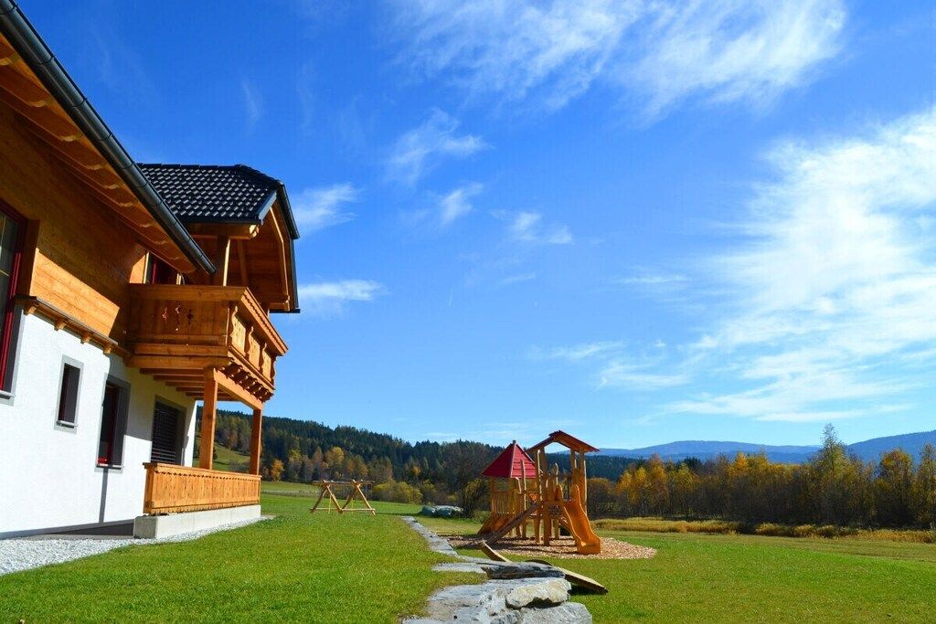 A wooden house with a balcony, a play area with a slide, and a clear sky.