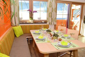 A dining area with a table set for four, a bench with cushions, and a window with curtains. - Holiday apartment Longa (Weißpriach)