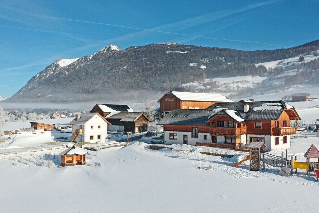 A snow-covered village with traditional wooden houses, a playground, and a mountain backdrop.