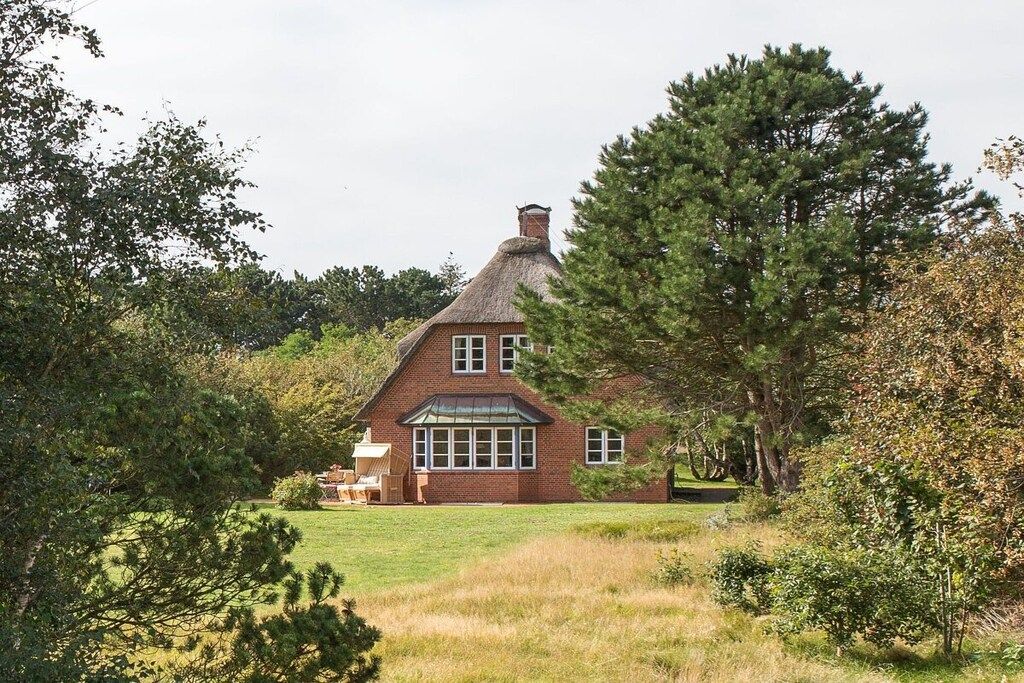 A brick house with a thatched roof, surrounded by trees and a grassy lawn.