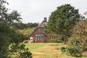 Ett hus byggt av tegel med ett halmtak, omgivet av träd och en gräsplätt.