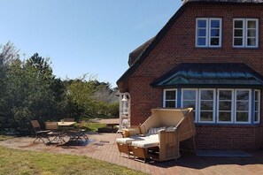Ein Backsteinhaus mit einer Terrasse, die Gartenmöbel und ein großes Fenster besitzt.