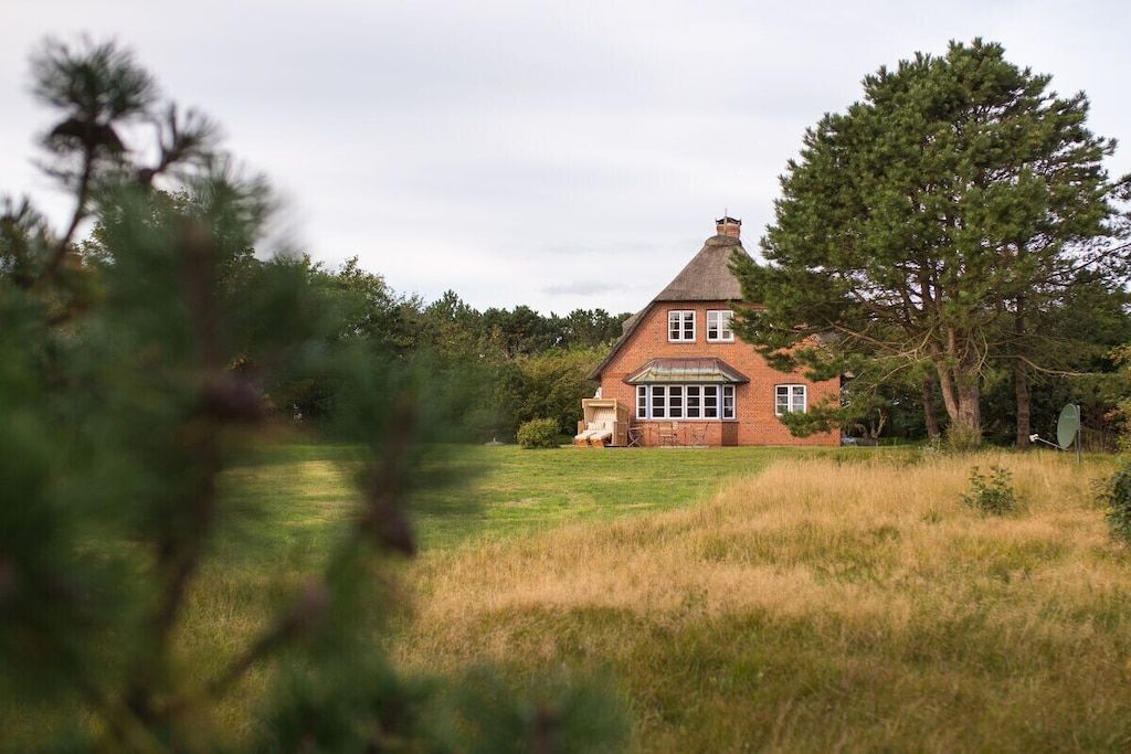 A brick house with a gabled roof, surrounded by grass and trees.