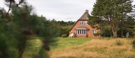 A brick house with a gabled roof, surrounded by grass and trees.