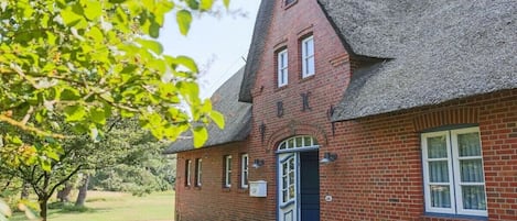 A brick building with a steeply pitched roof, a front door, and a small porch area.