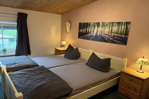 A bedroom with two beds, a nightstand with a lamp, a window with curtains, and a wall-mounted mirror. - Holiday home with 2 bedrooms (Joachimsthal)