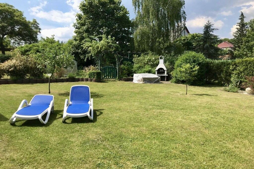 Een gazon met een achtertuin, twee blauwe lounge stoelen, een barbecue en een groene poort.