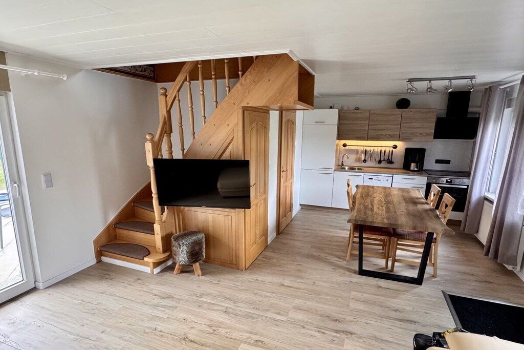A modern kitchen with wooden cabinets, a dining table, and a staircase with a built-in bench.