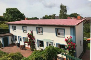 A two-story house with a red-tiled roof, a patio with chairs, and flowering plants. - Holiday home with 2 bedrooms (Joachimsthal)