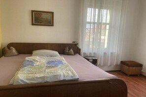 A bedroom with a bed, a bedside table, a nightstand, a window with curtains, and a painting on the wall. - Holiday apartment with 1 bedroom (Rhinow OT Kietz)