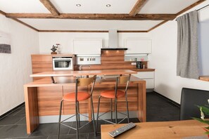 A modern kitchen with wooden cabinetry, a central island with bar stools, and a dining area with a table and chairs. - Edelweiss - Glacier Apartments (Flattach)