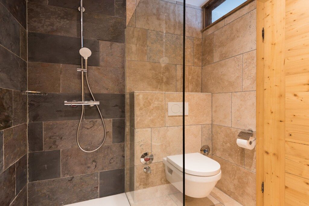 Een badkamer met een douche, toilet en een houten deur.