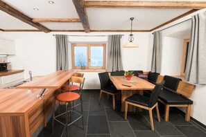 A modern kitchen with a wooden island, black chairs, and a dining table with chairs. - Edelweiss - Glacier Apartments (Flattach)