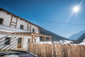 A white building with a wooden porch and a wooden fence, set against a mountainous backdrop. - Edelweiss - Glacier Apartments (Flattach)