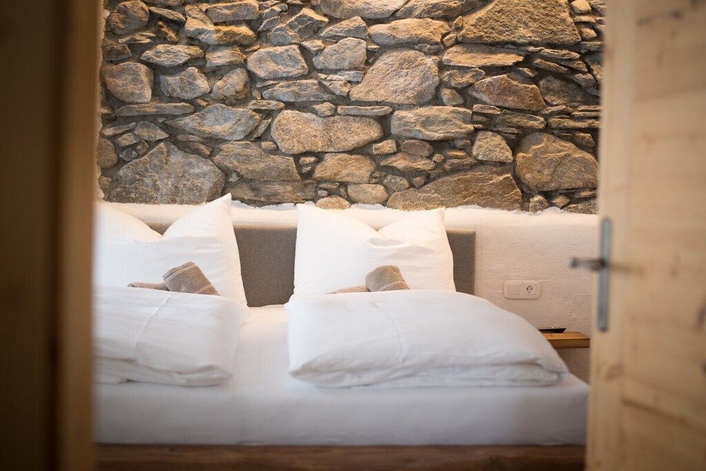 Ein Schlafzimmer mit einer Steinsandsteinwand, einem Bett mit weißer Bettwäsche und einer Holztür.