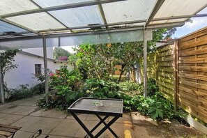 A covered patio area with a table, surrounded by plants and a wooden fence. - Holiday apartment with 1 bedroom (Flensburg)