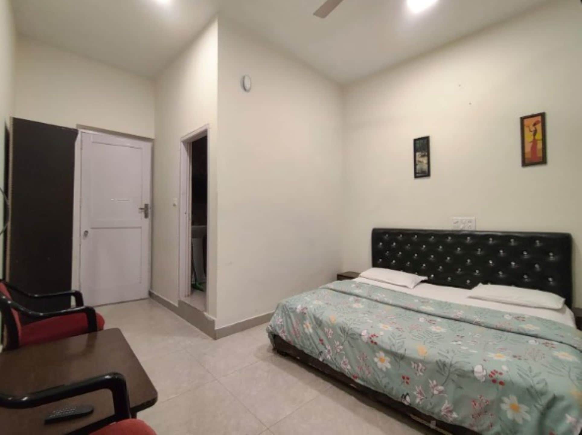 A bedroom with a bed, a chair, a door, and a small painting on the wall.