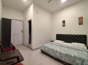 Un dormitorio con una cama, una silla, una puerta y un cuadro pequeño en la pared.