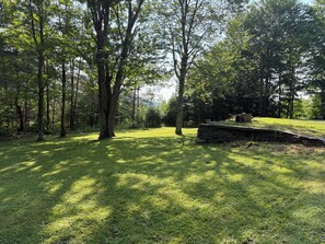 A grassy area with a stone bench and a small table, surrounded by trees. - Luxury Chalet on 1.5 Acres: Mountain Views, Hot Tub, Gym, fire pit & Ping-Pong (Windham)