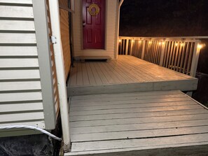 A wooden deck with a red door and a wreath, leading to a house with white siding. - Luxury Chalet on 1.5 Acres: Mountain Views, Hot Tub, Gym, fire pit & Ping-Pong (Windham)