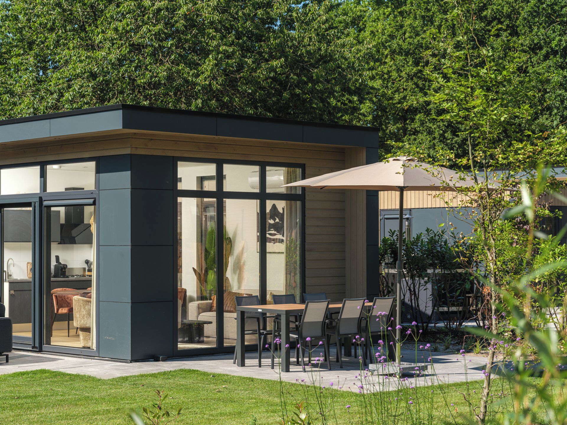 A modern outdoor dining area with a glass enclosure, a wooden deck, and a patio umbrella.