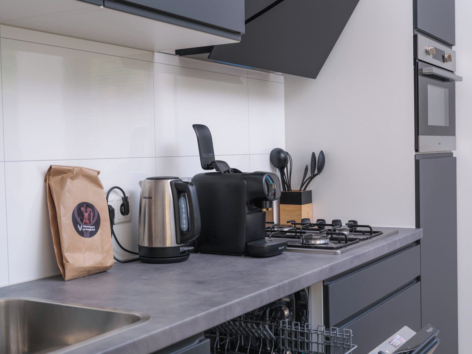Una cocina moderna con estufa a gas, cafetera, hervidor y una bolsa de café.