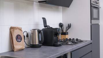 Una cocina moderna con estufa a gas, cafetera, hervidor y una bolsa de café.