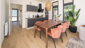 A modern kitchen with dark cabinets, a wooden dining table, and red upholstered chairs. - Stylish 6-person home with three bedrooms, a modern kitchen, air conditioning, a cozy outdoor space with a luxury pergola, private hot tub, sauna and a lounge area with an outdoor fireplace. Enjoy comfort and nature in the Veluwe. (Lieren)