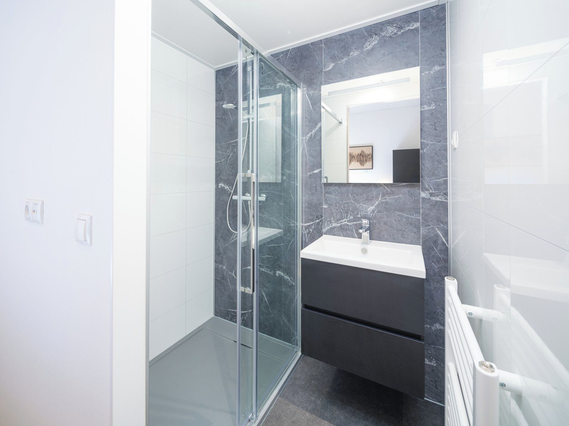 A modern bathroom with a glass shower enclosure, a dark vanity, and a white sink.