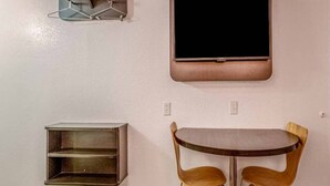 Een kamer met een aan de muur bevestigde televisie, een klein kastje en een tafel met twee stoelen.