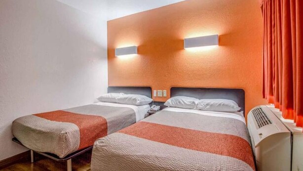 Een hotelkamer met twee bedden, een wandradiator en een raam met gordijnen.