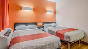 A hotel room with two beds, a heater, and a wall-mounted light fixture.