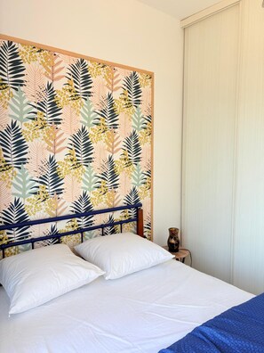 Ein Bett mit weißer Bettwäsche, einem blauen Kopfteil und einer Wand mit Blättermotiv.