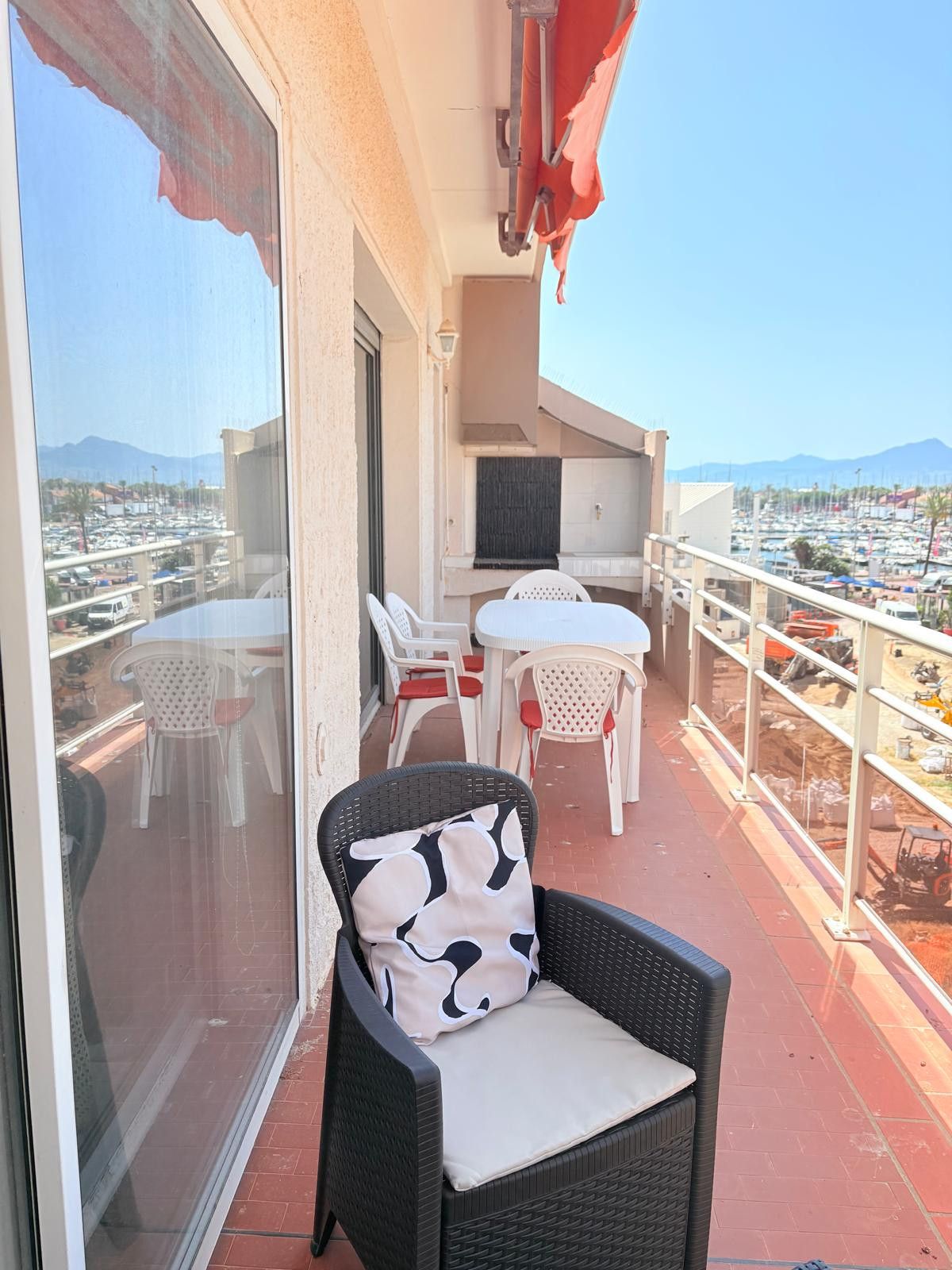 A balcony with a wicker chair, a table, and chairs with red cushions.