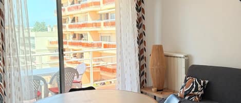 Ein modernes Wohnzimmer mit einem runden Holztisch, zwei schwarzen Stühlen, einem grauen Sofa und einem Kissen mit Muster. Eine besondere geometrische Pendelleuchte hängt von der Decke.