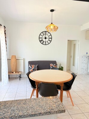 A modern dining area with a round table, black chairs, a wooden bench, a wall clock, and a hanging light fixture. - Superb apartment on the port of St Cyprien (Saint-Cyprien)