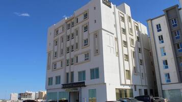 Um edifício de hotel com vários andares e fachada moderna, com vários espaços de estacionamento e um céu azul claro ao fundo.