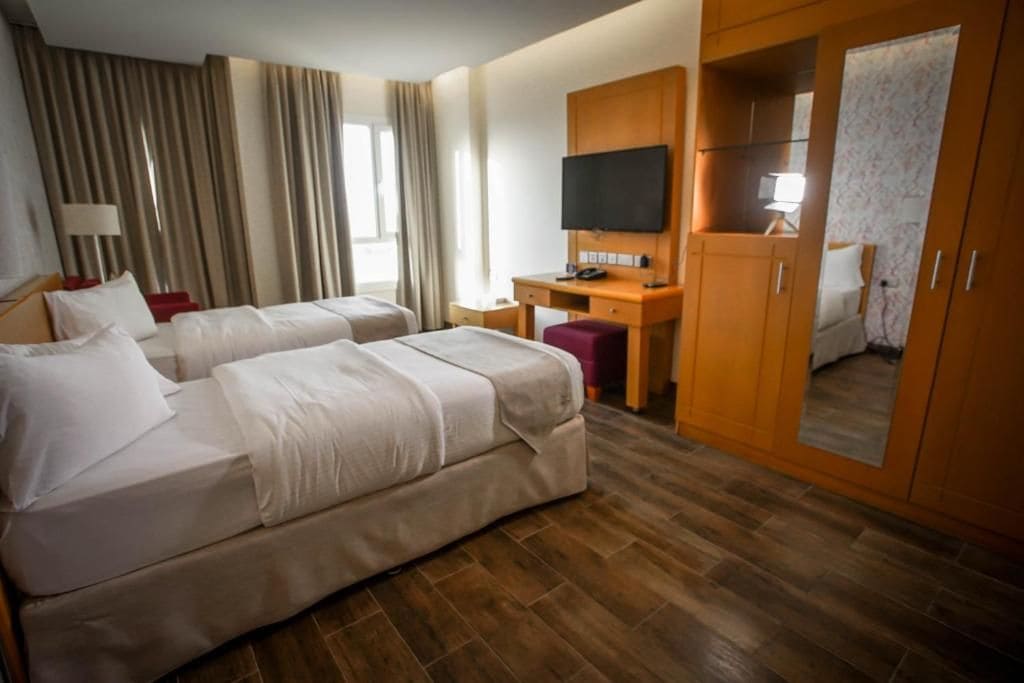 A hotel room with two beds, a desk, a television, and a wardrobe.