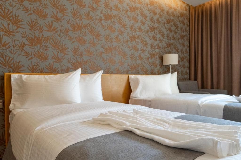 Een hotelkamer met twee bedden, een nachtkastje, een lamp en behang met een patroon.