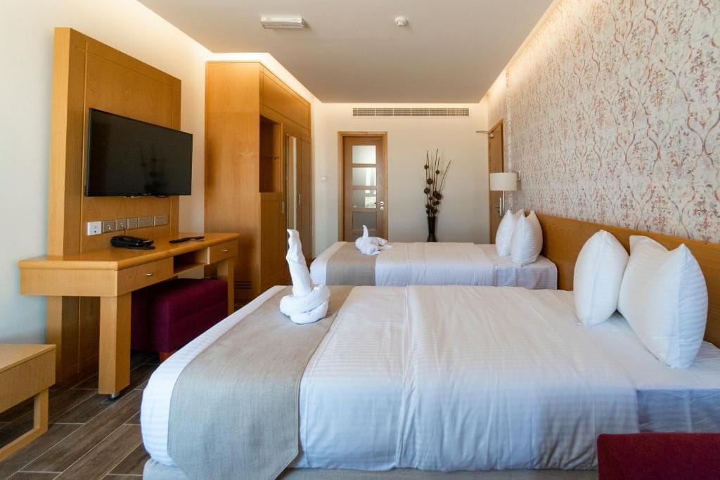 Ein Hotelzimmer mit zwei Betten, einem Schreibtisch, einem Fernseher und einem Spiegel.